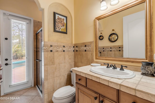 bathroom featuring tile patterned flooring, vanity, a shower with shower door, toilet, and tile walls