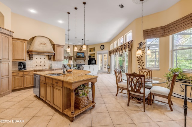 kitchen featuring sink, light stone counters, decorative light fixtures, backsplash, and an island with sink