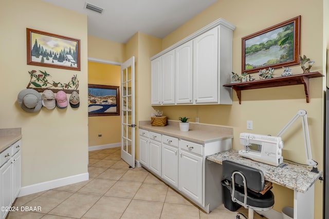 kitchen featuring light stone countertops, built in desk, light tile patterned flooring, and white cabinets