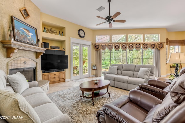 living room featuring light tile patterned flooring, a high ceiling, ceiling fan, built in features, and a tile fireplace