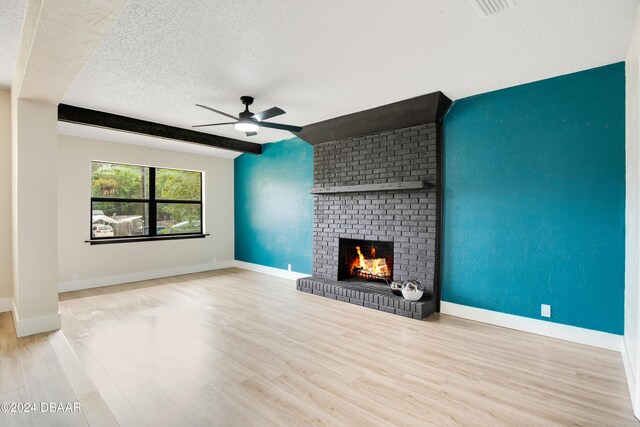 1512 Old Kings Rd, Daytona Beach, FL 32117 - unfurnished living room featuring light hardwood / wood-style flooring, ceiling fan, a fireplace, a textured ceiling, and beamed ceiling