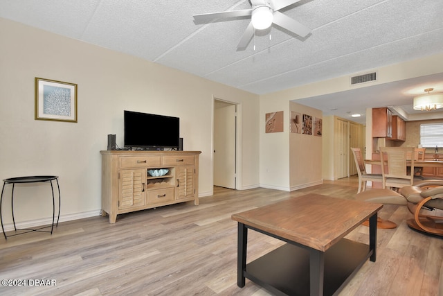 living room with a textured ceiling, ceiling fan, and light hardwood / wood-style flooring