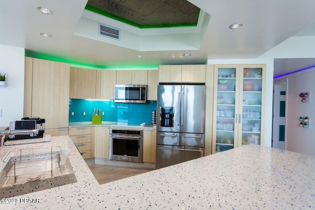 kitchen featuring light stone countertops, a raised ceiling, light wood-type flooring, and appliances with stainless steel finishes