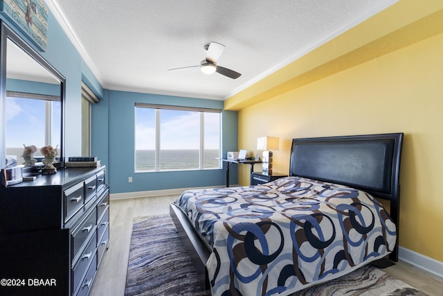 bedroom featuring crown molding, ceiling fan, a textured ceiling, wood finished floors, and baseboards