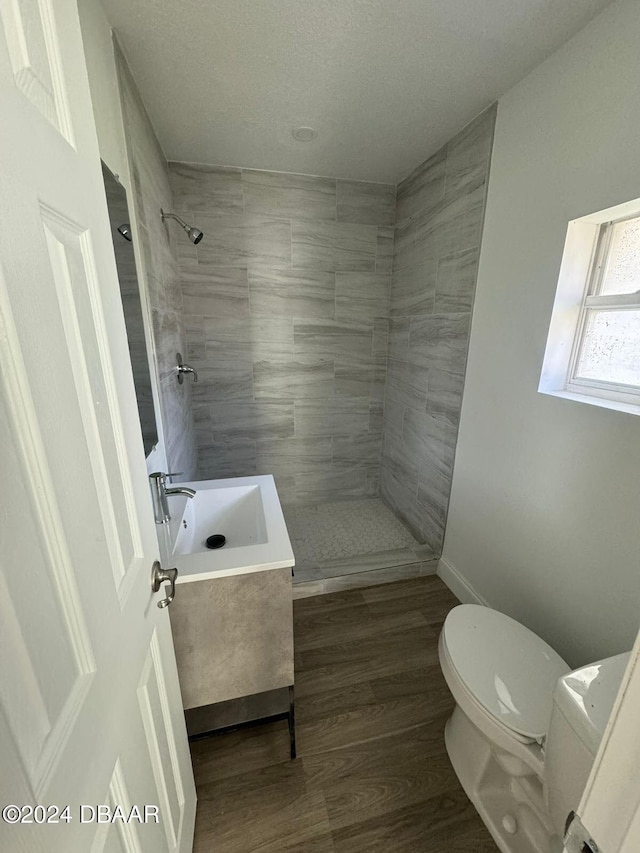 bathroom featuring a tile shower, hardwood / wood-style floors, vanity, and toilet