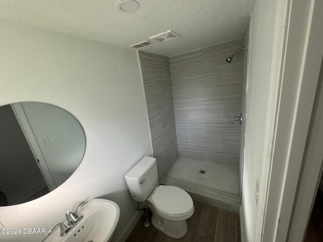 bathroom featuring hardwood / wood-style floors, a textured ceiling, a tile shower, and toilet