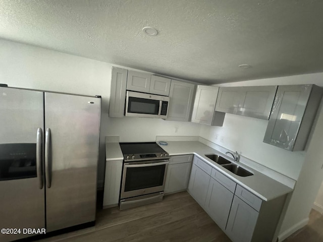 kitchen with appliances with stainless steel finishes, dark hardwood / wood-style flooring, a textured ceiling, sink, and gray cabinets