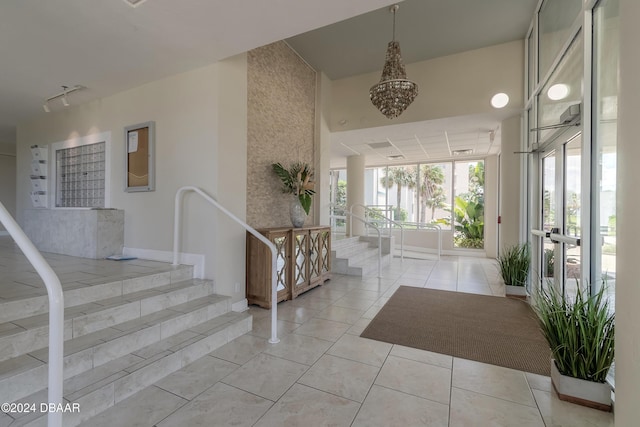 entrance foyer featuring light tile patterned floors, baseboards, a chandelier, stairway, and track lighting