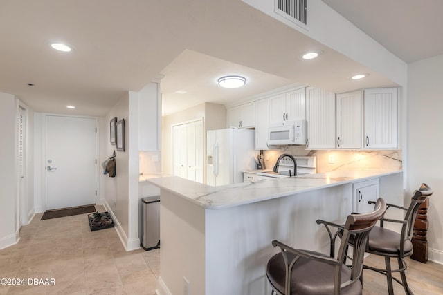 kitchen with backsplash, white appliances, a breakfast bar, white cabinets, and kitchen peninsula