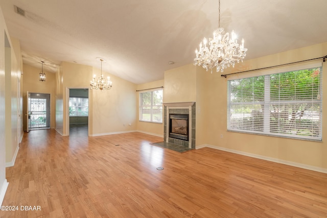 unfurnished living room featuring high vaulted ceiling, a fireplace, a notable chandelier, and light hardwood / wood-style flooring