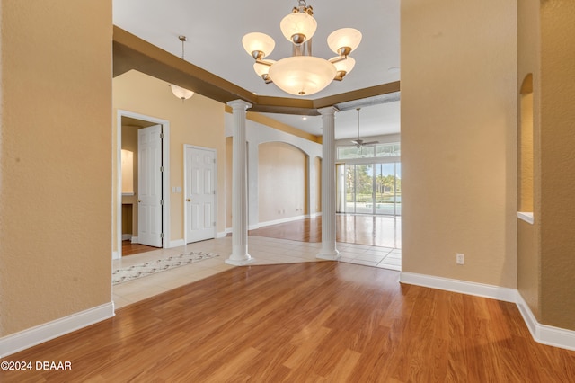 unfurnished room featuring ornate columns, ceiling fan with notable chandelier, and wood-type flooring