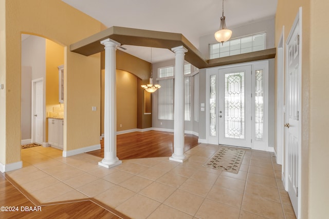 entryway featuring light wood-type flooring, a notable chandelier, and ornate columns