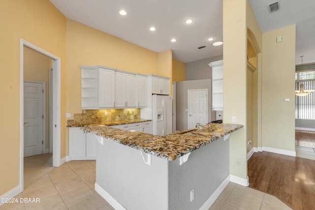 kitchen featuring white cabinets, stone countertops, kitchen peninsula, and white refrigerator with ice dispenser