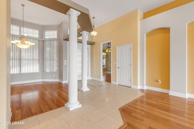 empty room featuring ornate columns, light hardwood / wood-style floors, and ceiling fan with notable chandelier