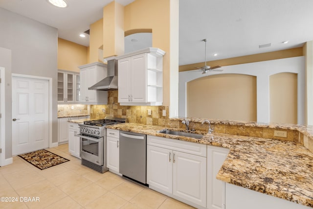 kitchen featuring white cabinets, sink, wall chimney range hood, light stone countertops, and appliances with stainless steel finishes