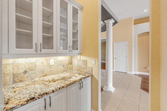 kitchen with light tile patterned floors, light stone countertops, decorative backsplash, white cabinets, and decorative columns