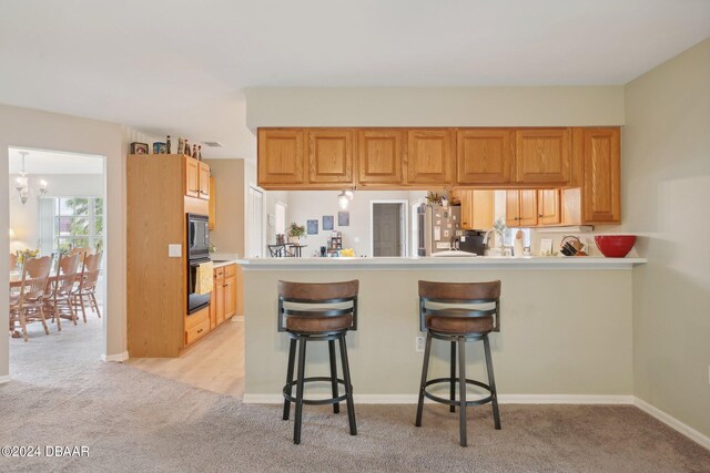 kitchen with stainless steel fridge, a notable chandelier, a breakfast bar area, kitchen peninsula, and light colored carpet