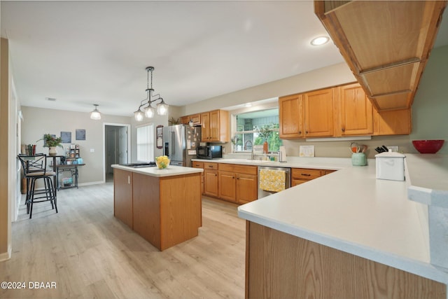 kitchen featuring sink, a kitchen island, light wood-type flooring, appliances with stainless steel finishes, and decorative light fixtures