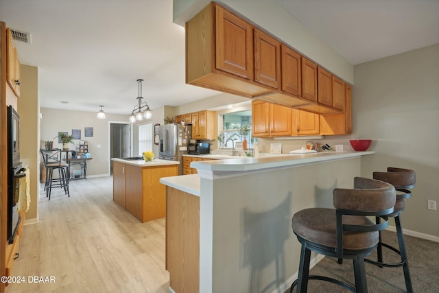 kitchen with stainless steel appliances, kitchen peninsula, a breakfast bar area, pendant lighting, and light hardwood / wood-style flooring