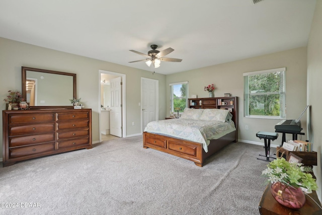 carpeted bedroom with ensuite bath, ceiling fan, and multiple windows