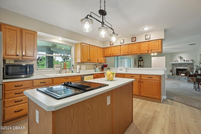 kitchen featuring sink, appliances with stainless steel finishes, decorative light fixtures, a stone fireplace, and a kitchen island