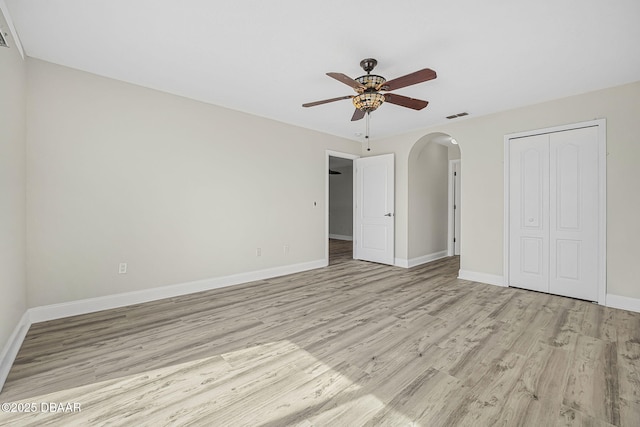 unfurnished bedroom featuring arched walkways, visible vents, baseboards, and light wood-type flooring