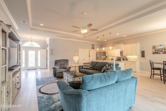 living room with ornamental molding, ceiling fan, light wood-type flooring, and a tray ceiling