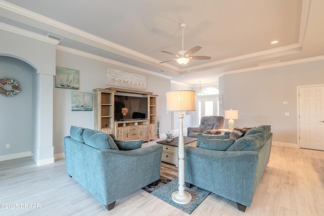 living room with ceiling fan, ornamental molding, a raised ceiling, and light wood-type flooring