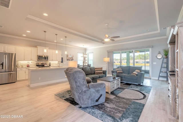 living room featuring crown molding, a tray ceiling, light hardwood / wood-style floors, and ceiling fan