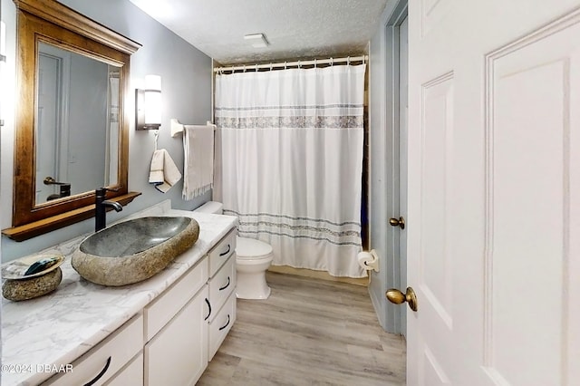 bathroom with wood-type flooring, a textured ceiling, toilet, vanity, and a shower with shower curtain