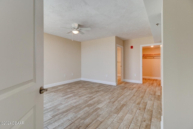 empty room featuring a textured ceiling, ceiling fan, baseboards, and light wood-style floors