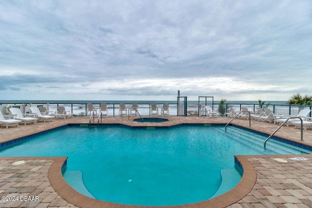 pool with a community hot tub, a water view, and a patio area