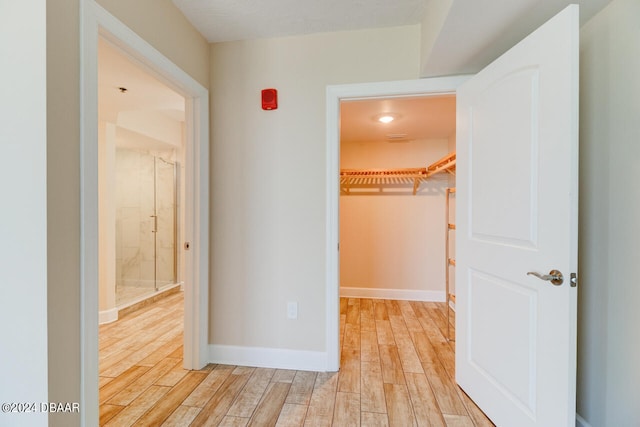 unfurnished bedroom featuring a spacious closet, a closet, light wood-style flooring, and baseboards