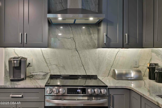 kitchen featuring stainless steel range with electric cooktop, gray cabinetry, light stone counters, tasteful backsplash, and wall chimney range hood