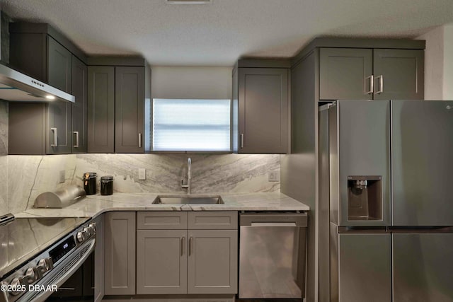 kitchen featuring sink, wall chimney range hood, stainless steel appliances, light stone counters, and tasteful backsplash