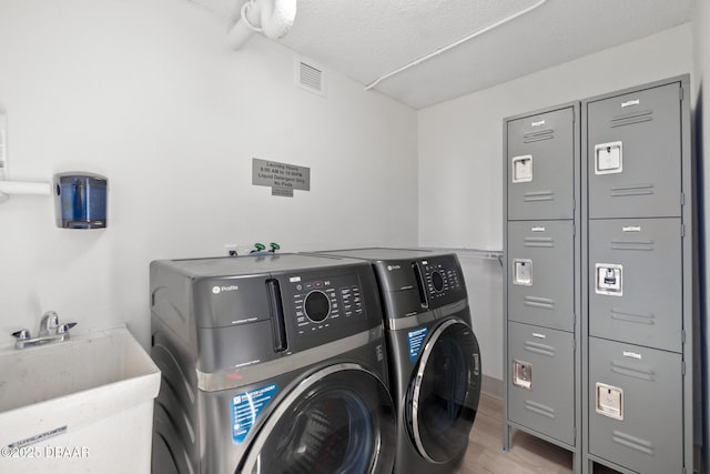 clothes washing area featuring sink, washing machine and dryer, a textured ceiling, and light wood-type flooring