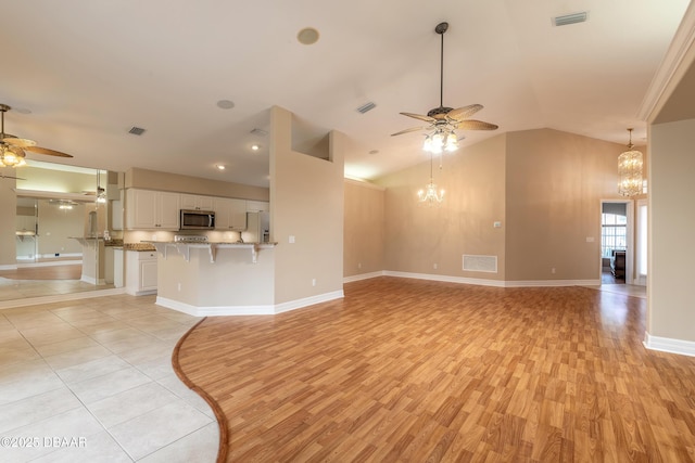 unfurnished living room featuring ceiling fan with notable chandelier, light hardwood / wood-style floors, and lofted ceiling