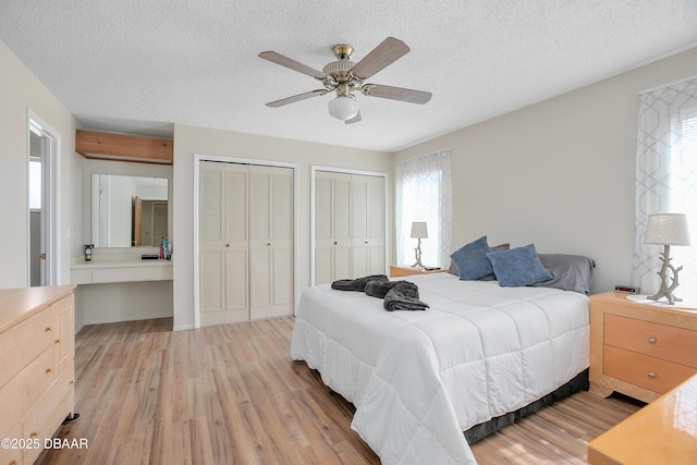 bedroom featuring ceiling fan, two closets, a textured ceiling, and light wood-type flooring