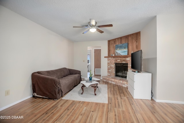 living room featuring ceiling fan, a fireplace, light hardwood / wood-style floors, and a textured ceiling