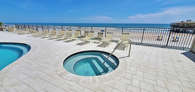 view of pool with a view of the beach, a patio, a water view, and a hot tub