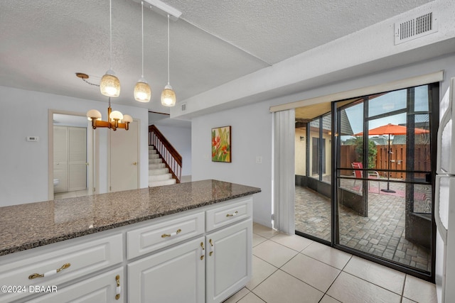 kitchen featuring a textured ceiling, light tile patterned floors, hanging light fixtures, white cabinets, and dark stone countertops