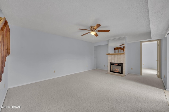 unfurnished living room with ceiling fan, a tiled fireplace, a textured ceiling, and light colored carpet