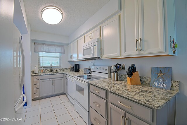 kitchen featuring light tile patterned floors, a textured ceiling, sink, light stone countertops, and white appliances