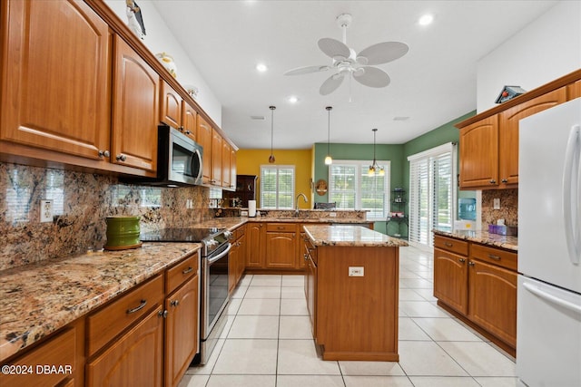 kitchen featuring stainless steel appliances, a kitchen island, hanging light fixtures, and light stone counters