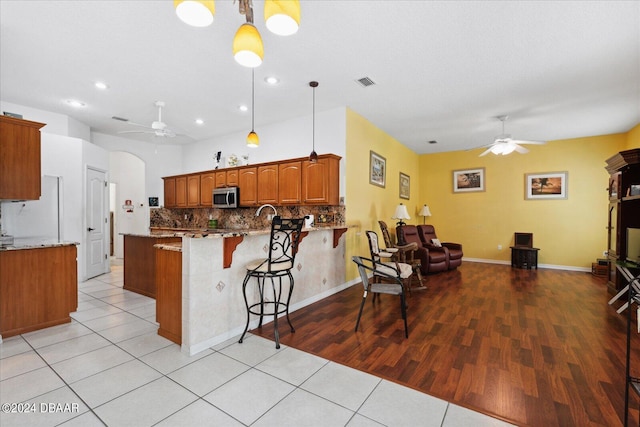 kitchen with pendant lighting, a kitchen breakfast bar, light wood-type flooring, light stone counters, and kitchen peninsula