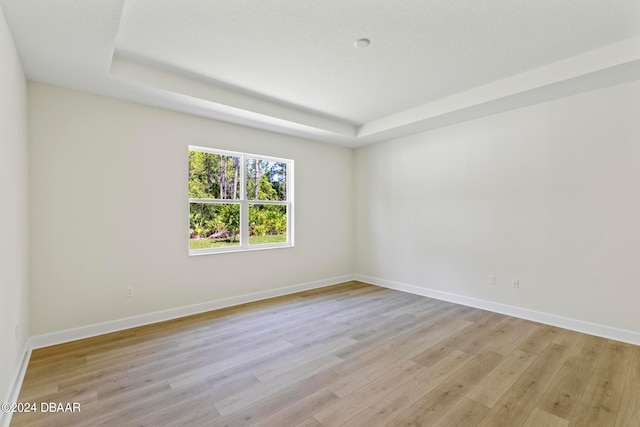 unfurnished room with light wood-type flooring and a tray ceiling