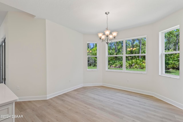 unfurnished dining area with light wood-type flooring, a healthy amount of sunlight, and an inviting chandelier