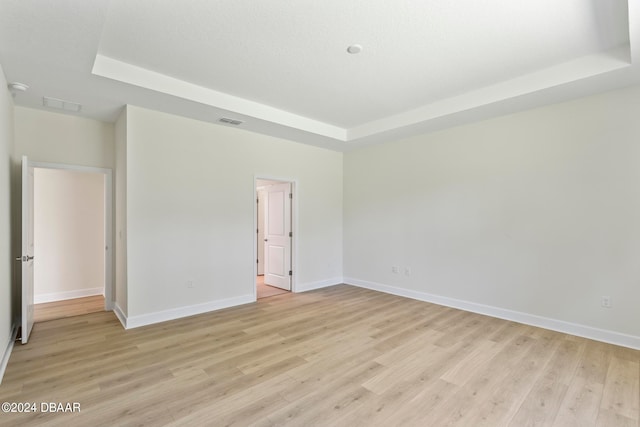 empty room featuring a raised ceiling and light wood-type flooring