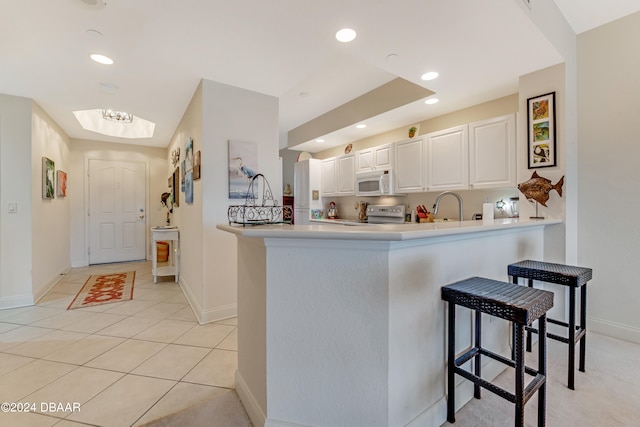 kitchen with white cabinets, white appliances, a kitchen bar, and kitchen peninsula