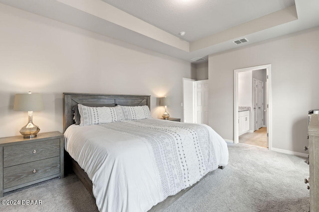 carpeted bedroom featuring connected bathroom and a tray ceiling